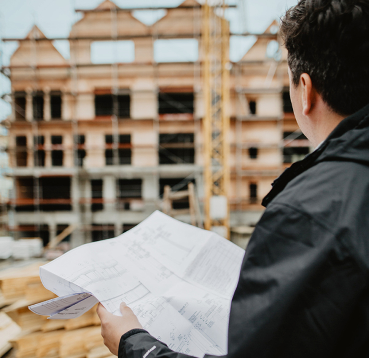 Immobilienentwickler mit Bauplan vor Baustelle